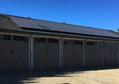 Large multi-car garage with 6 white barn-style garage doors and solar panels covering the dark roof.