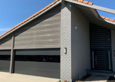 Contemporary home with dark gray garage doors featuring glass panels, brick accent wall, and terracotta roof tiles.